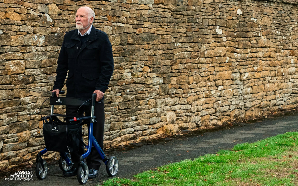 Older man out walking with the Electric Blue Rehasense Space LX rollator in front of a dry stone wall