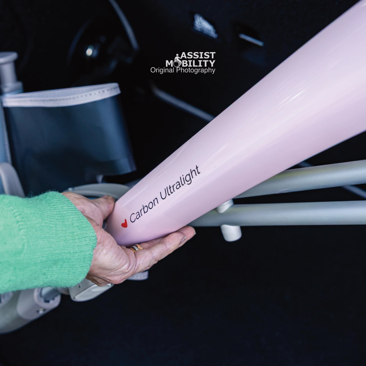 Hand holding the Pale Rose carbon fibre frame of the byACRE Carbon Ultralight rollator, with the Carbon Ultralight logo