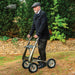 Older man in a flat cap walking up a grassy slope with a byACRE Carbon Overland off-road rollator