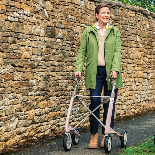 Woman walking with the Pale Rose byACRE Carbon Ultralight rollator along a path beside a Cotswold stone wall