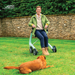 Smiling woman sitting on the seat of a Glacier Green byACRE Nordic Pioneer rollator in a garden, with her dog lying on the grass
