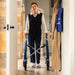 A woman using a blue byACRE Nordic Pioneer rollator in a home hallway, wearing a black vest over a white shirt and dark trousers.