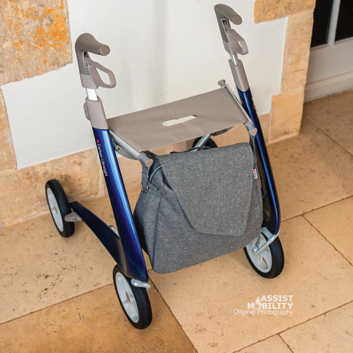 Grey byACRE Weekend Bag fitted under the seat of a blue byACRE Carbon Ultralight rollator, shown from the front on a stone floor