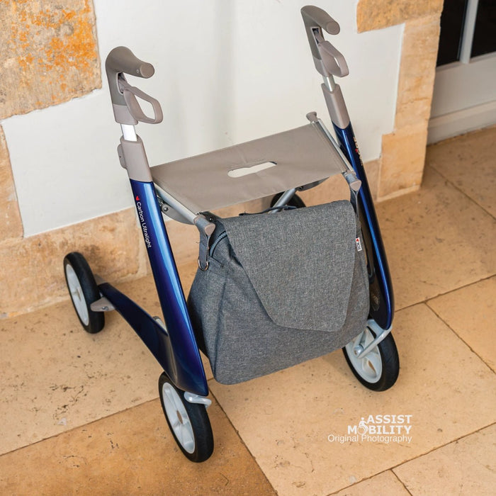 Grey byACRE Weekend Bag fitted under the seat of a blue byACRE Carbon Ultralight rollator, shown from the front on a stone floor