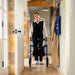 A woman pushes a blue Rehasense Space LX rollator with a shopping basket in a bright, traditional hallway with stone walls and hanging coats.