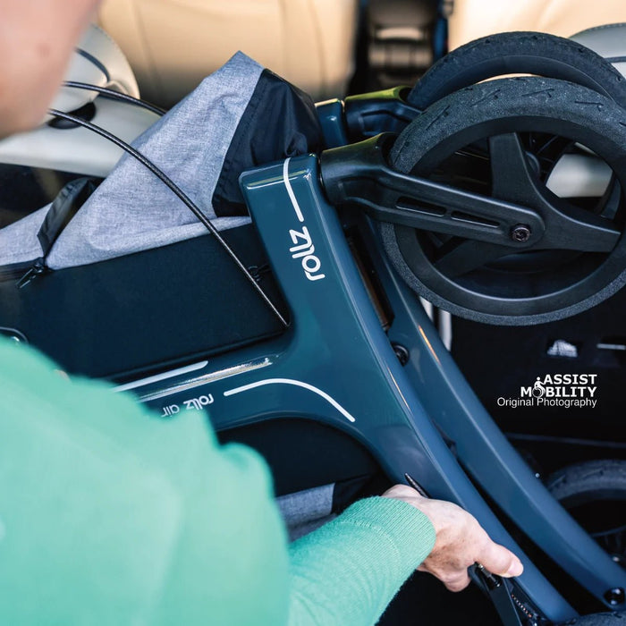 Over-the-shoulder view of a woman loading the folded Rollz Air Carbon Fibre rollator into a car, showing the frame and Rollz logo