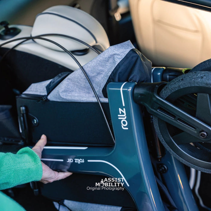 Hand holding the dark teal carbon fibre frame of the folded Rollz Air Carbon Fibre rollator, showing the Rollz Air logo
