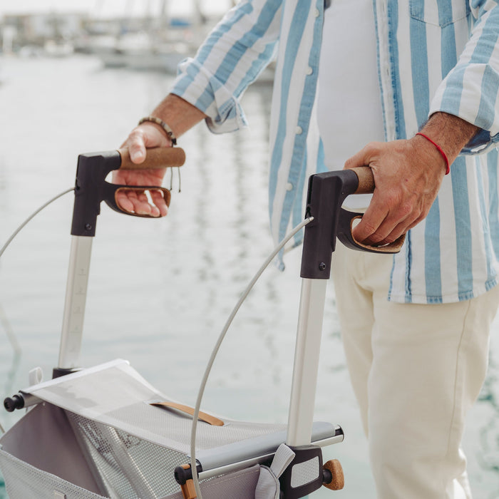 A close up of a person holding the cork handles and brake levers of a Saljol Allround Rollator Superlight in Ice Blue 