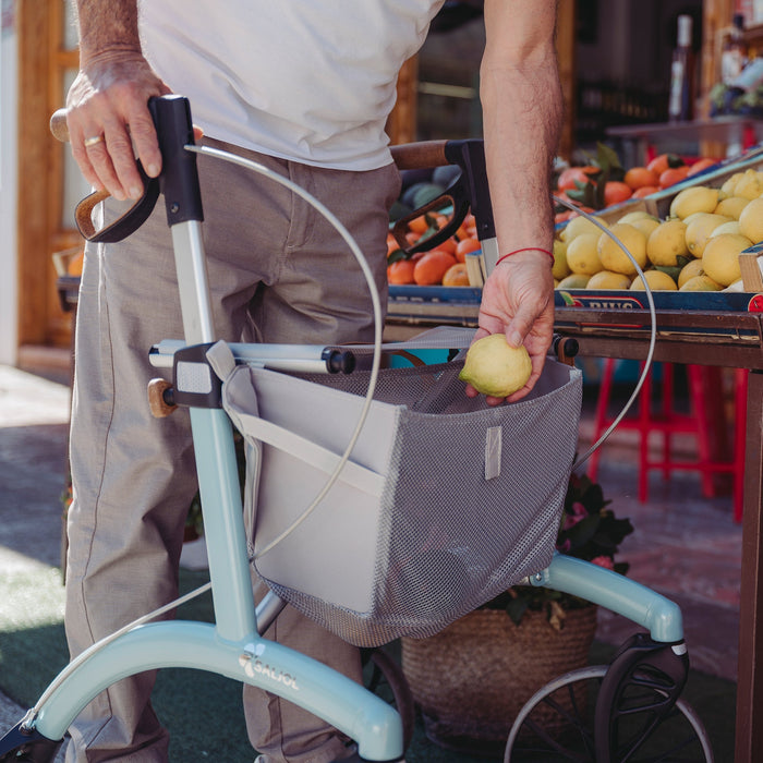 A person grocery shopping with the Saljol Allround Rollator Superlight in Ice Blue putting a lemon into the mesh bag