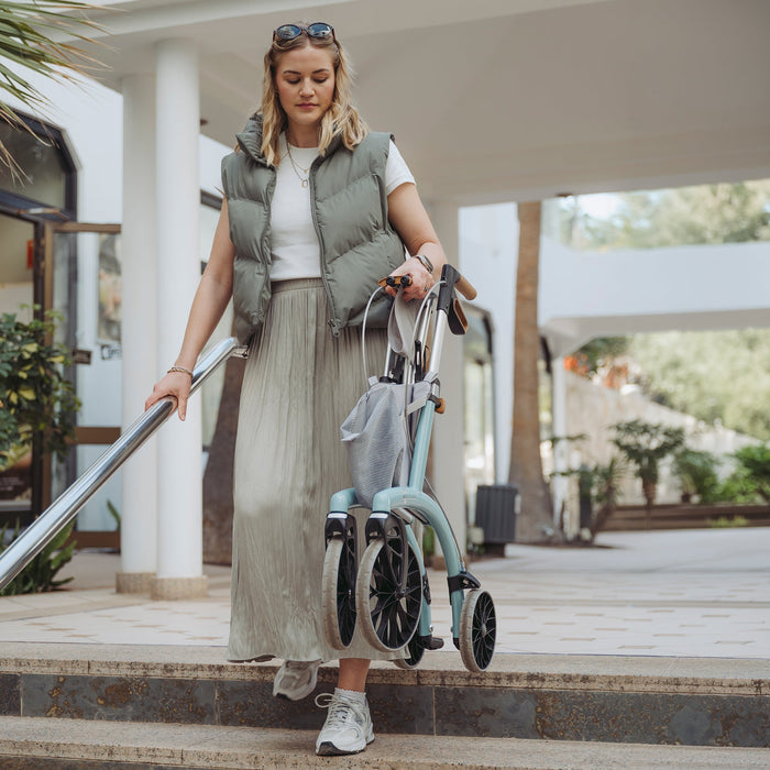 A lady carrying with one hand the Saljol Allround Rollator Superlight Ice Blue rollator down the stairs.