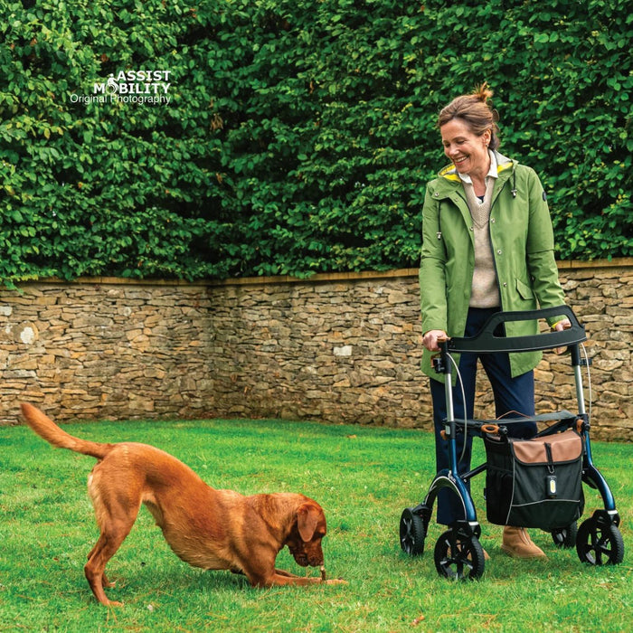 Laughing woman standing with a Saljol Carbon Fibre rollator in her garden while her dog plays on the lawn