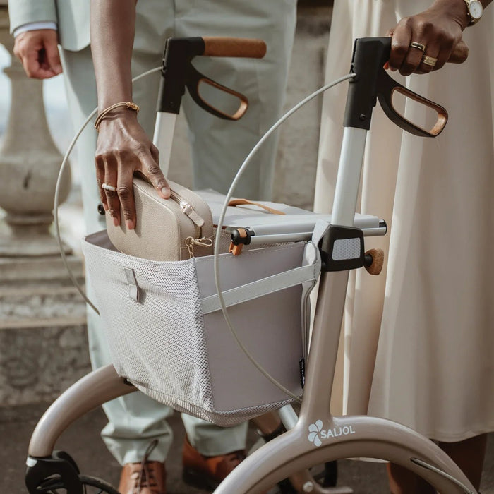 Close-up of a woman placing her handbag in the mesh shopping bag of a Saljol Carbon Superlight rollator