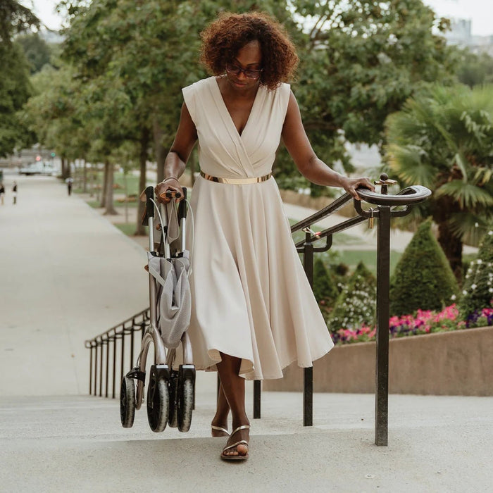 Woman holding the handrail on outdoor park steps while bringing her folded Saljol Carbon Superlight rollator with her