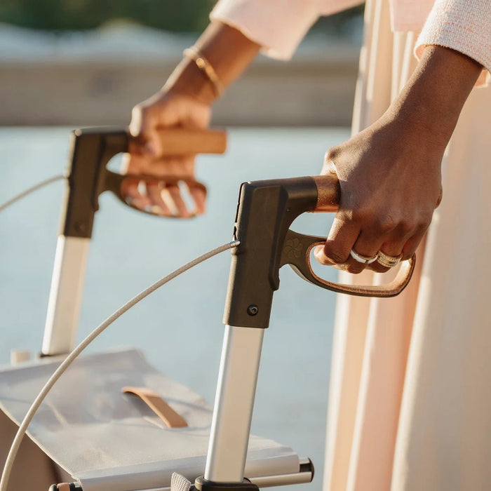 Close-up of both hands gripping the ergonomic handles and brake levers of the Saljol Carbon Superlight rollator