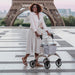 Smiling woman walking with a Rose Gold Saljol Carbon Superlight rollator at the Trocadéro in Paris, with the Eiffel Tower behind her