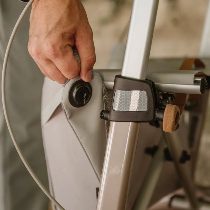 Close-up of a hand fastening the bag attachment on the frame of a Saljol Carbon Superlight rollator, next to the reflector
