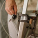 Close-up of a hand fastening the bag attachment on the frame of a Saljol Carbon Superlight rollator, next to the reflector