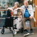An elderly couple seated next to the Troja Original Black Series rollator. 