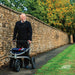Older man out walking with the Trionic Veloped Sport rollator on a path between a stone wall and autumn trees