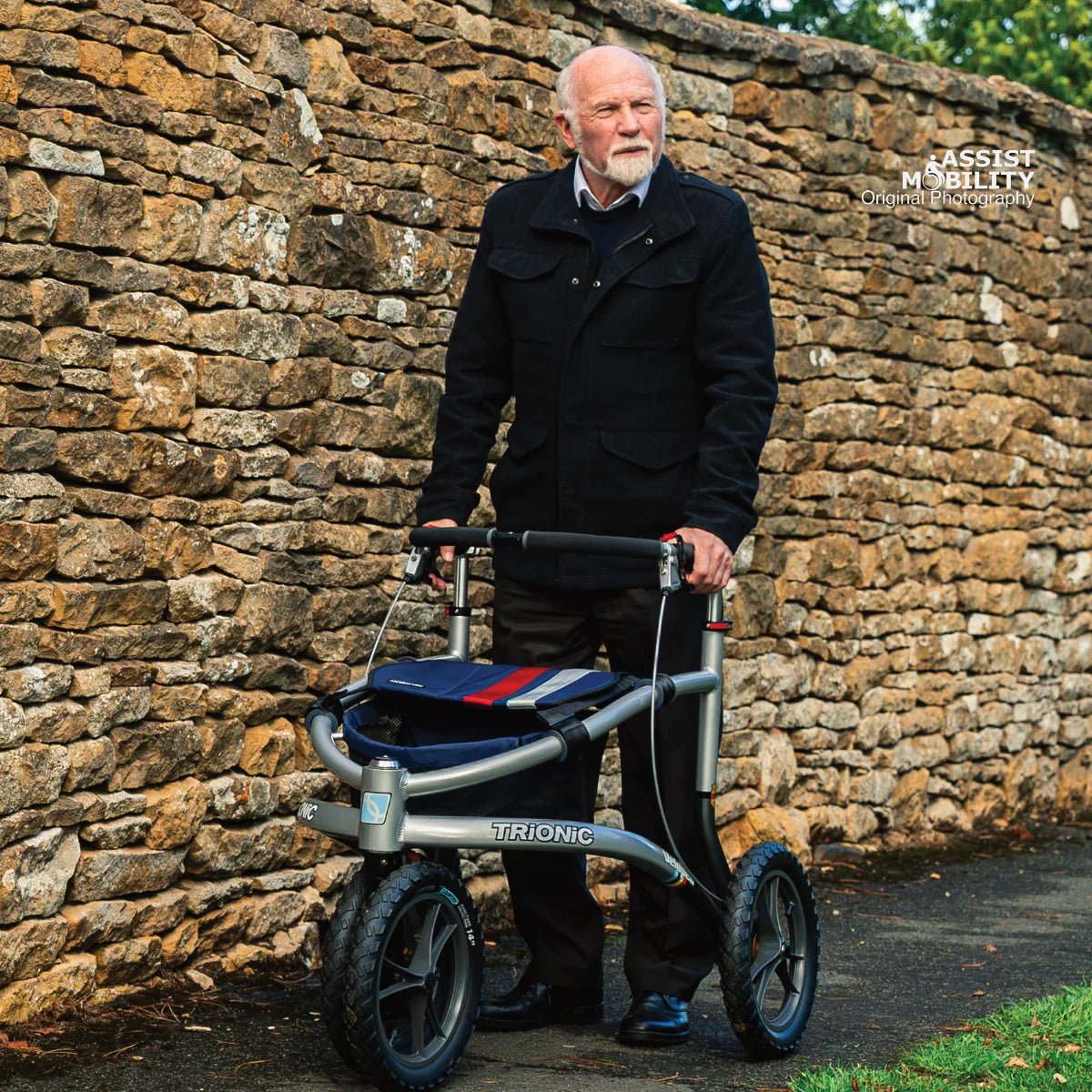 Older man standing behind the Trionic Veloped Sport off-road rollator in front of a dry stone wall