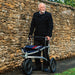 Older man standing behind the Trionic Veloped Sport off-road rollator in front of a dry stone wall