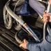 A close-up of a person loading a silver Trionic Veloped rollator into the boot of the car. The wheel is removed to save space. 