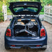 The compact folded Trust Care Let's Fly rollator in the boot of a dark blue Mini Cooper on a gravel driveway