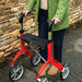 Close-up of the red Trust Care Let's Fly rollator with its built-in seat, Trust logo and large wheels