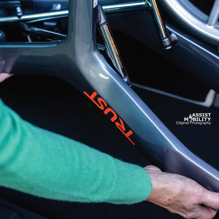 Hands holding the metallic grey Trust Care Let's Fly rollator frame, showing the red Trust branding