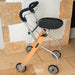 A folding Trust Care Let's Go Indoor rollator with a light wood frame, silver metal tubing, black seat and handle grips, and four wheels, photographed indoors against a stone and plaster wall.