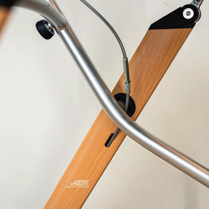 A close-up of a Trust Care Let's Go Indoor rollator brake cables, positioned against a beige stone and white wall background.