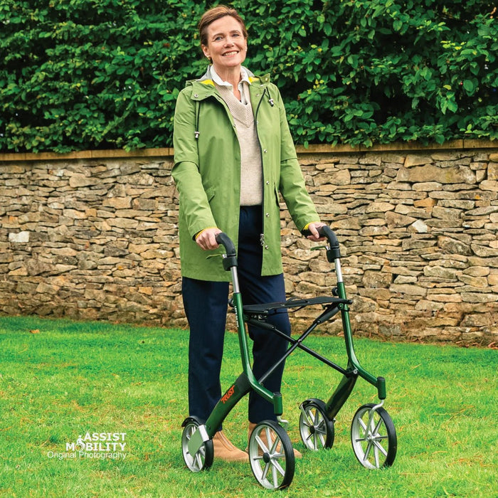 Woman smiling with her British Racing Green Trust Care Let's Go Out rollator, showing its seat and large wheels on a lawn
