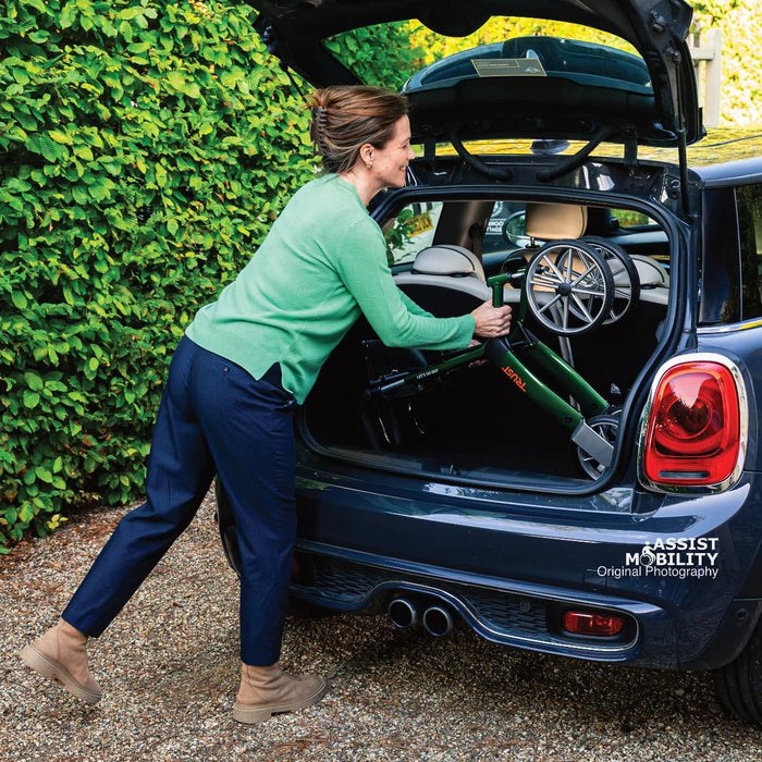 Smiling woman loading the folded British Racing Green Trust Care Let's Go Out rollator into the boot of a Mini Cooper