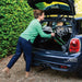 Smiling woman loading the folded British Racing Green Trust Care Let's Go Out rollator into the boot of a Mini Cooper
