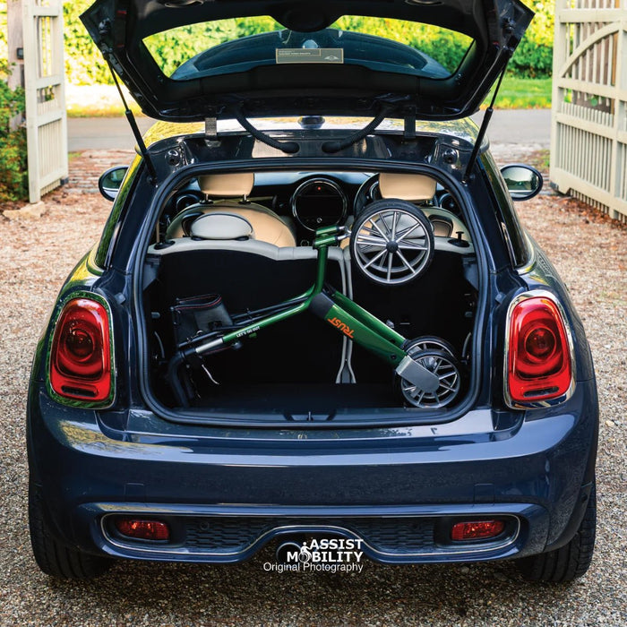 British Racing Green Trust Care Let's Go Out rollator folded in the boot of a dark blue Mini Cooper on a gravel driveway