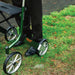 Close-up of the British Racing Green Trust Care Let's Go Out rollator frame, showing the Trust logo, seat and spoked wheels on grass