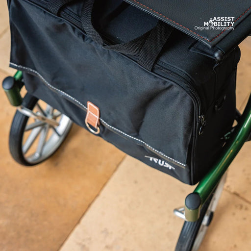 Angled side view of the black Trust Care Let's Go Out rollator bag with reflective stitching, under the seat of the green rollator