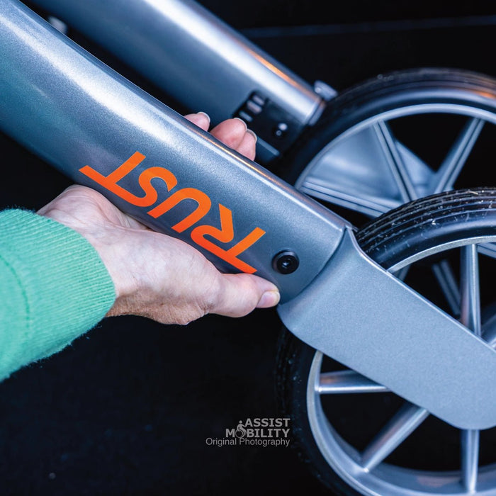 Hand holding the silver aluminium frame of the Trust Care Let's Shop rollator, showing the orange Trust branding