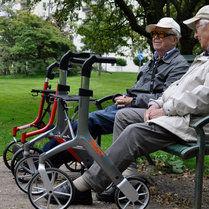 Two gentlemen chatting on a park bench with their Let's Fly rollators ready and waiting. 