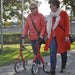Two ladies walking side by side with a Red Lets Fly rollator with colour cordinated coats.