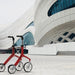 Red Lets Fly rollator standing along in front of a dramatic modern building.